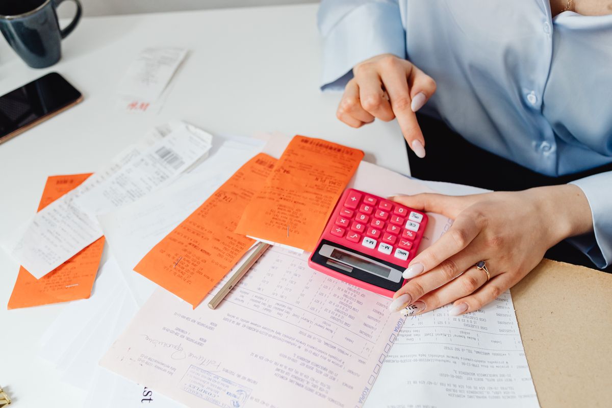 A calculator, printed invoices and receipts spread across a wooden desk