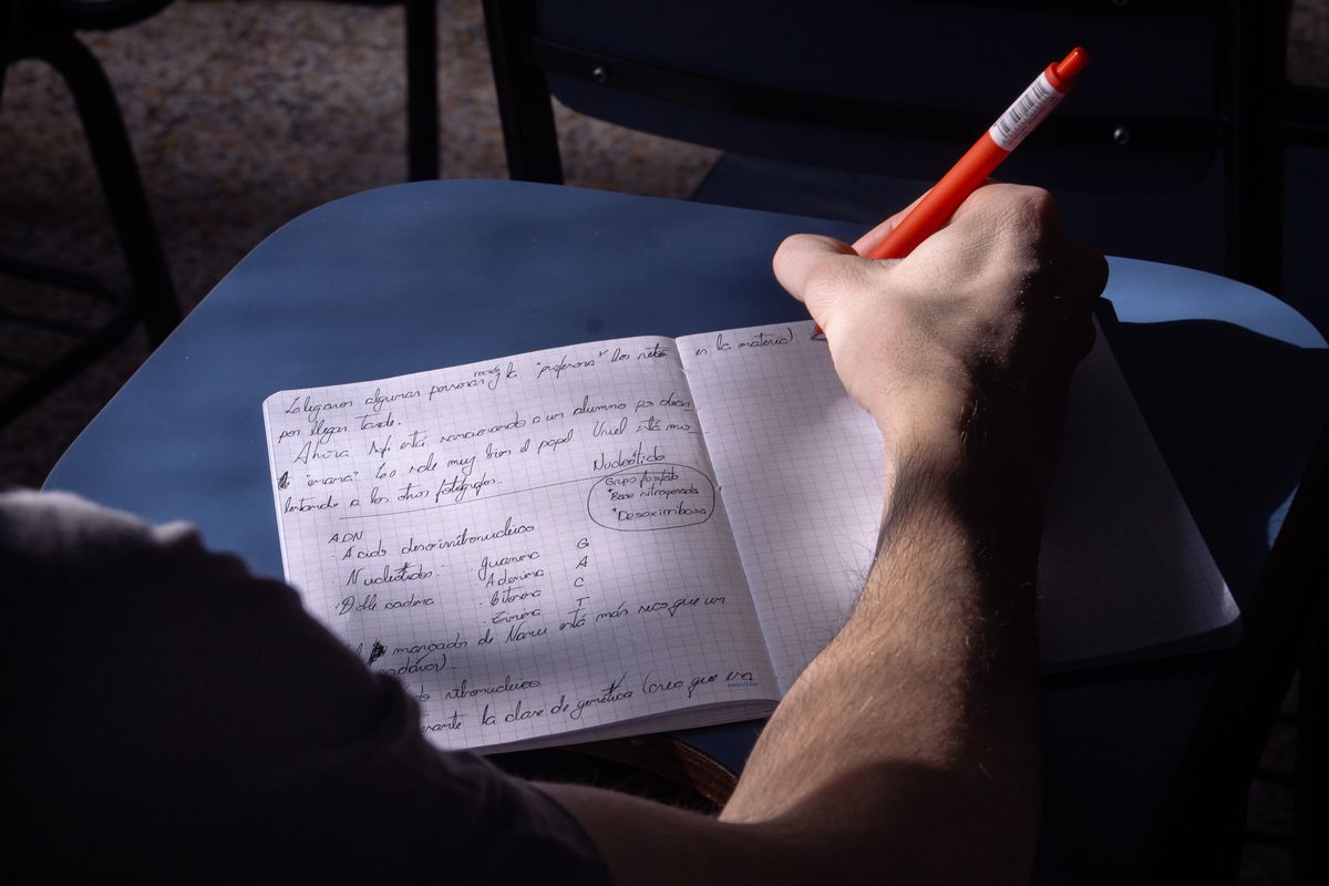 Hands writing short notes by hand in a lined notebook beside a coffee cup