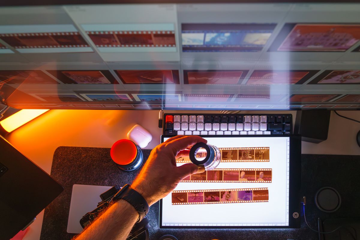 A hand holding a loupe over a strip of film frames on a light table