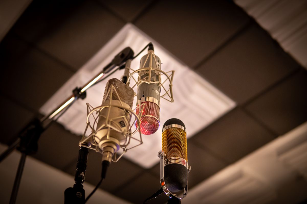 Three studio microphones on stands in a treated recording booth