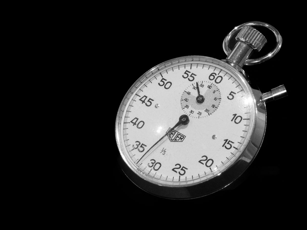 A hand holding a stopwatch with a thumb on the button
