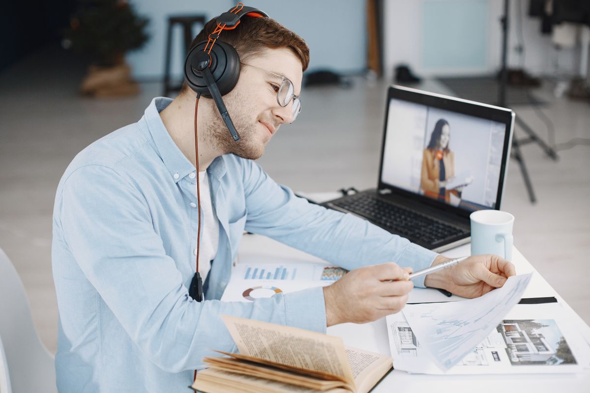 A reviewer watching a video closely on a laptop with headphones on