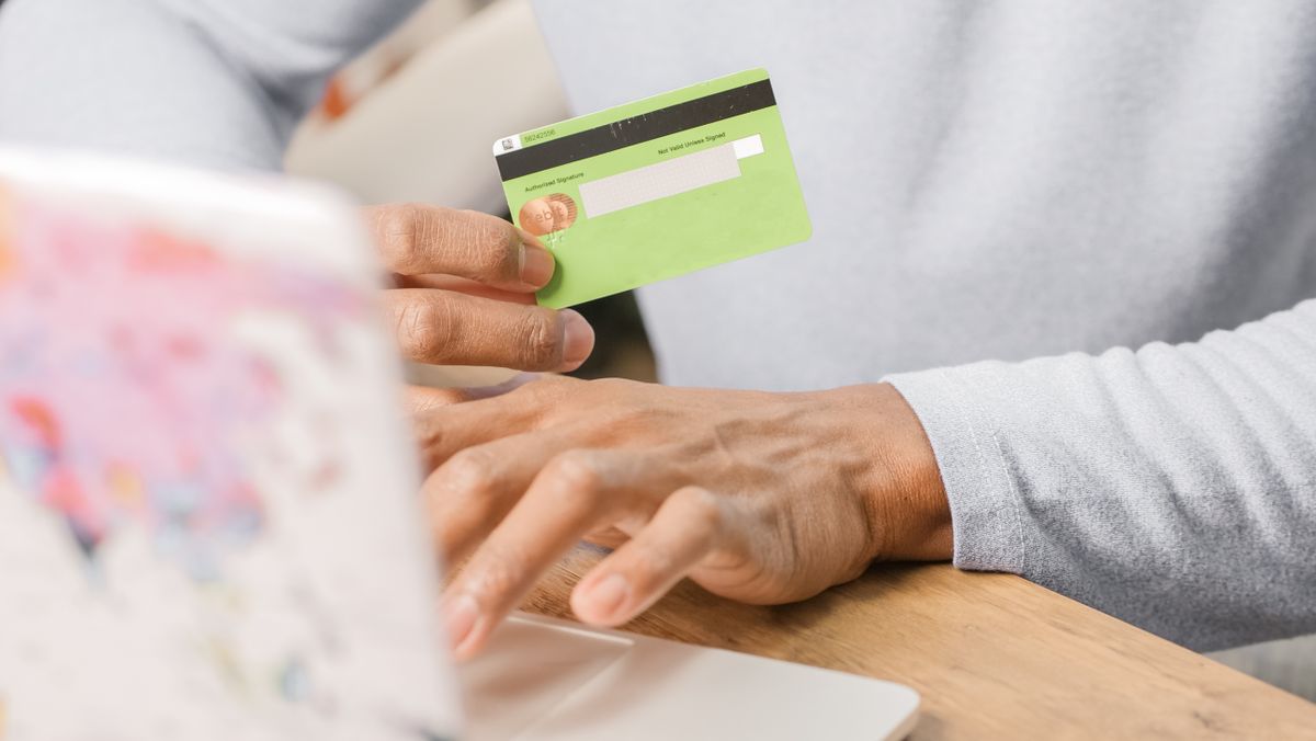 Hands holding a bank card in front of an open laptop