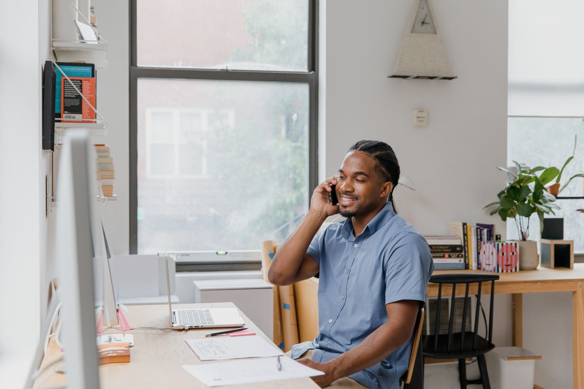 A person taking a phone call at a desk beside a laptop and a page of notes