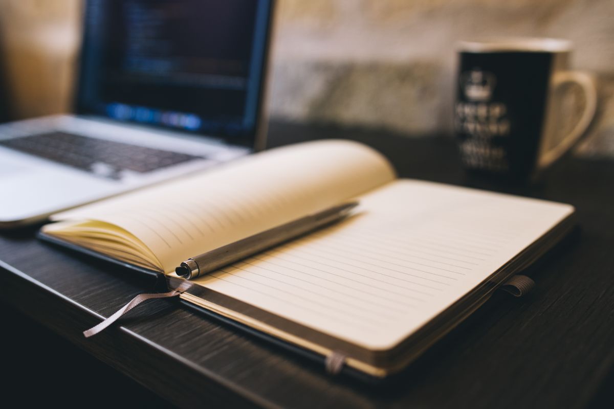 A notebook open beside a laptop, mid-decision